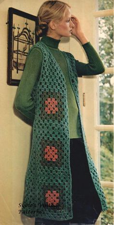 a woman standing in front of a window wearing a green crocheted cardigan