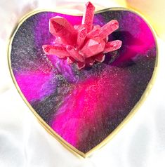 a heart shaped box with pink and purple flowers in it's center on a white surface