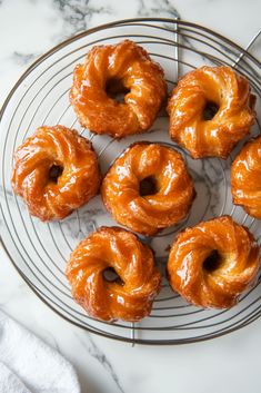 six glazed doughnuts on a wire rack sitting on a marble counter top, ready to be eaten