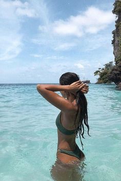 a woman standing in the ocean with her hand on her head looking into the distance