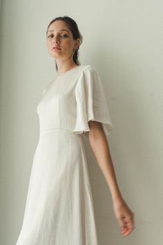 a woman standing in front of a wall wearing a white dress with ruffle sleeves