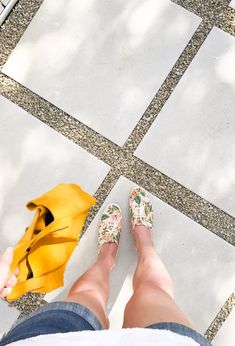 a woman's feet with floral shoes and yellow bag on the ground next to her