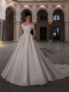 a woman in a white wedding dress standing in a large room with columns and arches