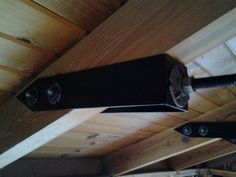 a black speaker hanging from the side of a wooden ceiling in a room with wood paneling