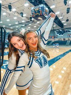 two cheerleaders pose for a photo on the court with their arms in the air