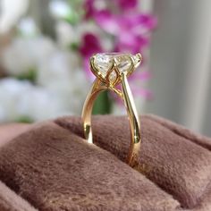 a gold ring sitting on top of a brown velvet box with flowers in the background