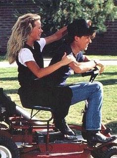 a man riding on the back of a red lawn mower next to a woman