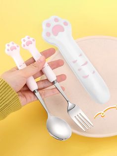 a person holding two forks and spoons in front of a plate with paw prints on it