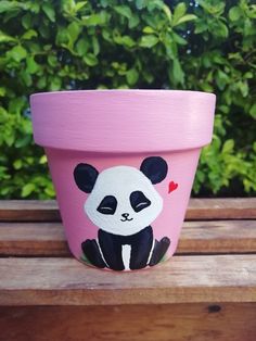 a pink flower pot with a panda face painted on the side, sitting on a wooden bench