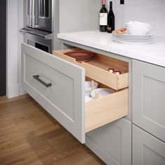 an open drawer in the middle of a kitchen with plates and wine bottles on it