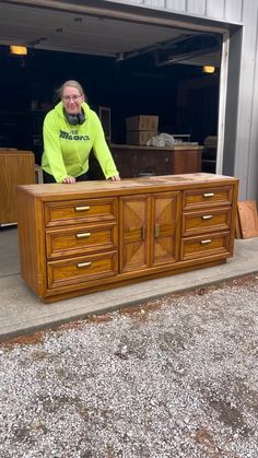 a man standing behind a wooden dresser in front of a garage door with his hands on the drawers