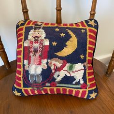 a needlepoint pillow on a wooden chair with a santa riding a sleigh