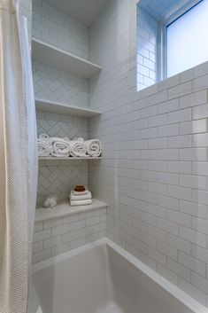 a white tiled bathroom with shelves and towels on the shelf above the bathtub area