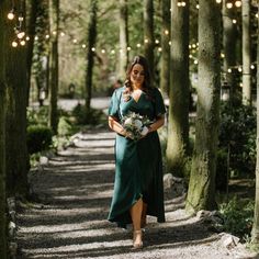 a woman in a green dress is walking through the woods with lights strung above her