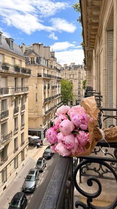 a bunch of pink flowers sitting on top of a balcony next to a street filled with cars