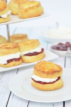 some scones with jam and cream on them are sitting on white plates next to other pastries