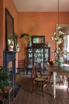 a dining room with orange walls and wooden flooring, an old fashioned table surrounded by chairs