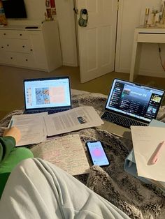 three laptops and papers on a bed with someone's feet in the middle