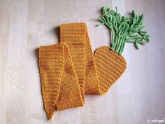 an orange knitted mitt next to a green leafy plant on a wooden surface