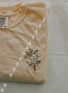 a t - shirt with flowers embroidered on the front and back, sitting on a white surface