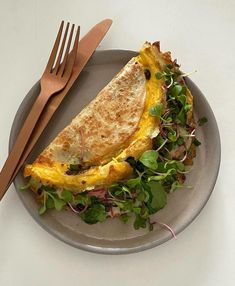 an omelet is on a plate next to a fork and knife, along with some greens