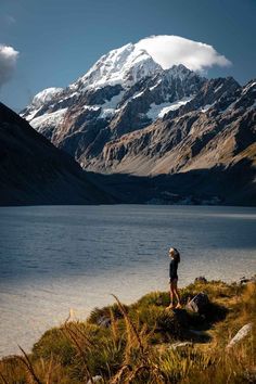 a person standing on top of a grass covered hill next to a body of water