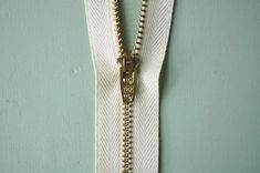 a white zipper with gold metal teeth on a mint green wall, showing the bottom part of the zipper