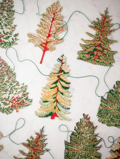 several different types of christmas trees on a white tablecloth with red and green thread