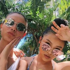 two young women wearing sun glasses standing next to each other with palm trees in the background