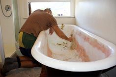 a man in brown shirt and green pants cleaning a white bathtub with red stains