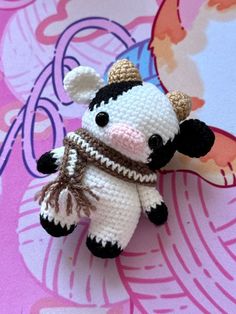 a small crocheted cow with a scarf around it's neck sitting on a pink surface