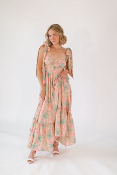 Introducing the Icebreaker Maxi Dress, a captivating blend of elegance and charm. This dress features a bold pink floral print that exudes vibrant appeal, perfect for making a statement. The adjustable bow straps add a touch of whimsy and femininity, while the flattering smocked bodice ensures a perfect fit. The flowing maxi skirt provides stunning movement, making every step a show stopping moment. Pink Maxi Dress With Square Neck For Garden Party, Pink Square Neck Maxi Dress For Vacation, Floral Print Dress With Ruffled Straps For Brunch, Spring Garden Party Dresses With Bow, Pink Maxi Dress With Ruffled Straps For Vacation, Spring Beach Dress With Bow Detail, Spring Beach Dress With Bow, Garden Party Maxi Dress With Tie Straps, Spring Flirty Maxi Dress With Tie Back