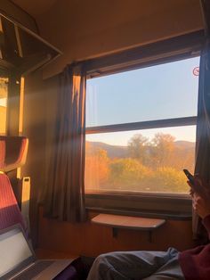 a person sitting on a train looking at their cell phone and laptop in front of the window