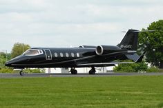 a black jet sitting on top of an airport tarmac next to grass and trees