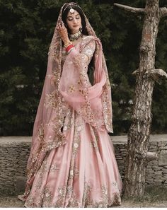 a woman in a pink wedding dress standing next to a tree and wearing a veil