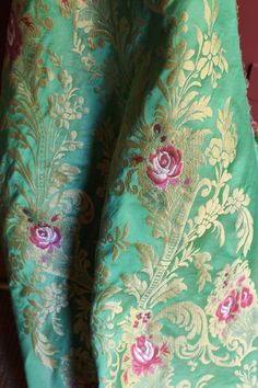 the fabric is green and gold with pink flowers on it's side, as well as an intricately designed design