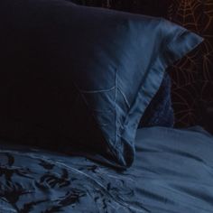 a bed with blue sheets and pillows on top of it in front of a spider web wallpaper