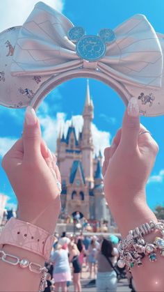 two hands holding up a minnie mouse ears in front of a castle with people walking around