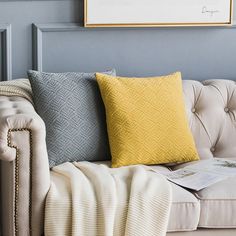 a couch with yellow and grey pillows on it in front of a blue wall,