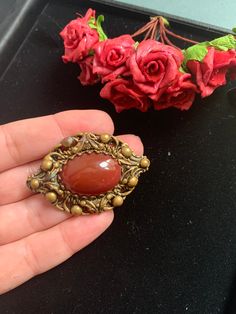 Andriani Vintage is pleased to offer for sale this wonderful example of a Carnelian Colour Cabochon brooch. It has a large central maroon colour cabochon stone  Mounted on a decorative brass like metal alloy base. In an Victorian style  MEASUREMENTS  Size is 5 x 4cms CONDITION In nice vintage condition some minor greening on the brass but nothing that detracts from the original design of this piece  Great unusual item at a very affordable price. Real must have for collectors and fashionistas ali Vintage Gemstone Round Brooches, Vintage Oval Brooch With Cabochon, Vintage Oval Cabochon Brooch, Unique Cabochon Brooches As Gift, Antique Pendant Brooch With Cabochon, Pendant Brooch With Cabochon For Gift, Handmade Victorian Oval Brooches, Handmade Vintage Red Brooches, Handmade Bohemian Brooches For Collectors