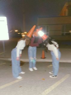 three people standing in the middle of a parking lot with traffic cones on their heads