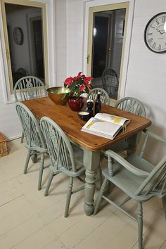 a wooden table with chairs around it and a clock on the wall behind it,