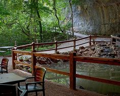 an outdoor dining area with tables and chairs next to a river in the woods,