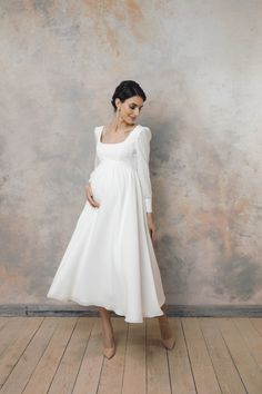 a pregnant woman wearing a white dress standing in front of a wall