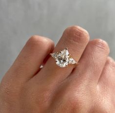 a woman's hand holding an engagement ring with three diamonds on it and the middle finger