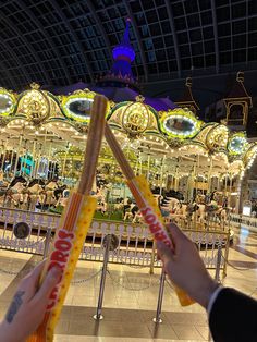 two people holding candy sticks in front of a merry go round