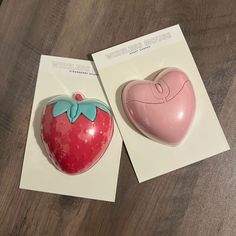 two strawberry shaped magnets sitting next to each other on top of a wooden table