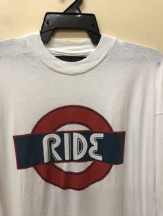 a white t - shirt with the word ride on it hanging from a hanger