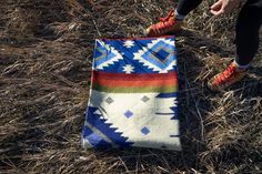 a person standing next to a colorful blanket on the ground with their feet propped up