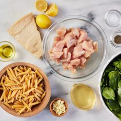 ingredients to make pasta salad laid out on a marble counter top with lemons, olives, and other foodstuffs